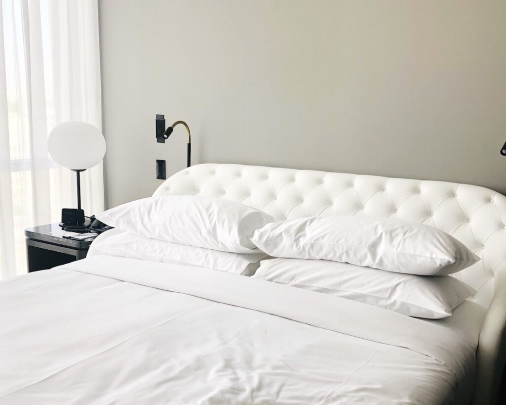 An comfy bed with all white bedding in a hotel room. Always get an early hotel check in with our hotel booking strategy.
