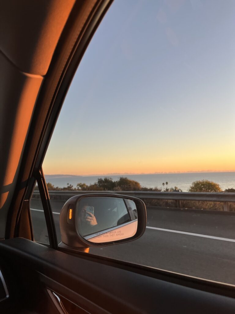 Our list of 11 Pismo Beach Hotels you should consider for your next beach vacation.

This image is a photo taken from a car as the photographer is driving along the coast near Pismo Beach. You can see the sun setting over the Pacific Ocean.